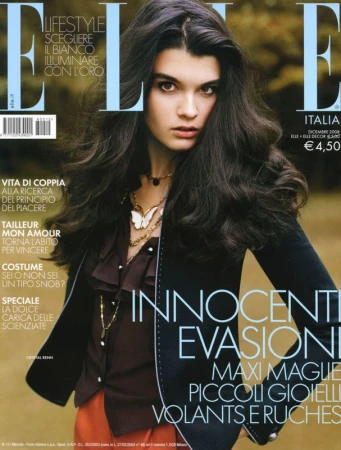Magazine cover featuring a dark-haired woman with voluminous hair wearing a ruffled dark blouse and jacket with layered gold necklaces.