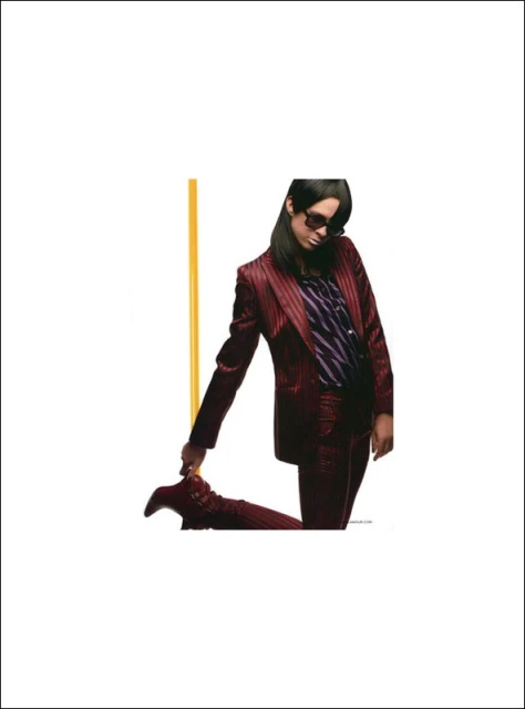 Woman in burgundy pinstripe suit poses with sunglasses and matching boots against white background with vertical gold bar.