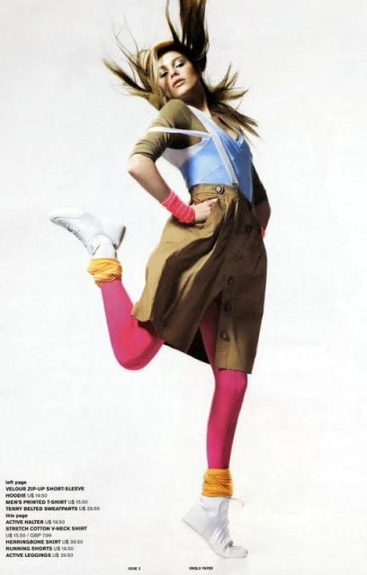 Fashion editorial shot of a woman in pink leggings, a khaki skirt, and white high-top sneakers leaping against a white background.