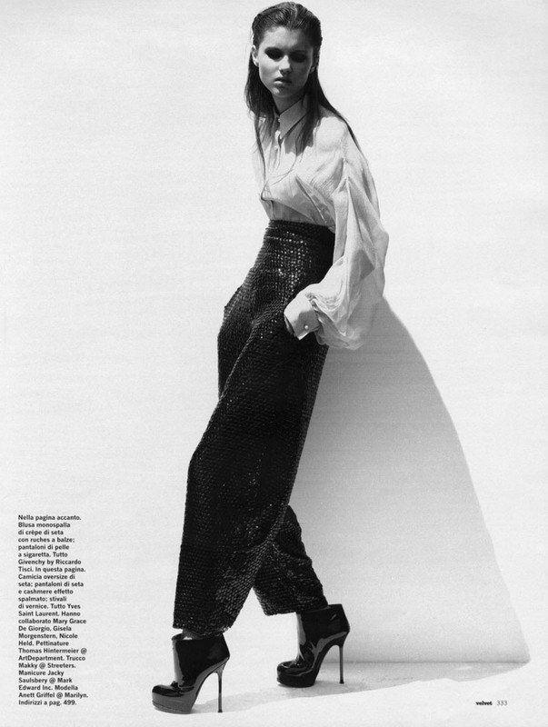 Fashion editorial shot of a young adult woman with dark hair wearing high-waisted sequin pants, a blouse, and platform heels in a studio.