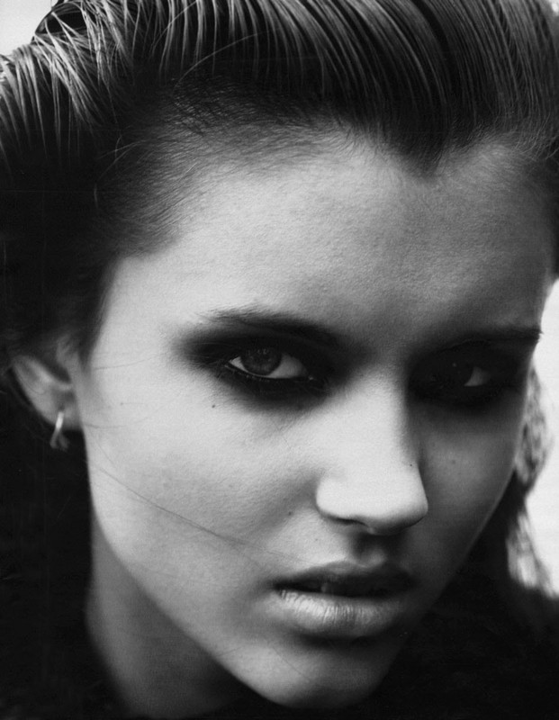 Monochrome close-up portrait of an adult female with dark hair, heavy smoky eye makeup, and hoop earrings, staring intensely at the camera.