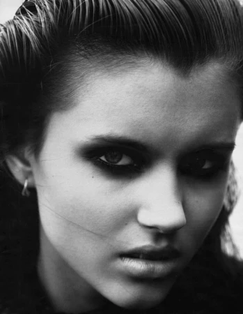 Monochrome close-up portrait of an adult female with dark hair, heavy smoky eye makeup, and hoop earrings, staring intensely at the camera.