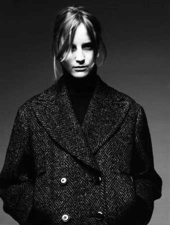 Monochrome portrait of a woman wearing a patterned double-breasted tweed coat and a dark turtleneck sweater