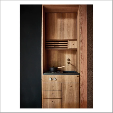 Minimalist kitchen design with light wood cabinetry, black countertops, a cooking pot on the stove, and a black wall on the side.
