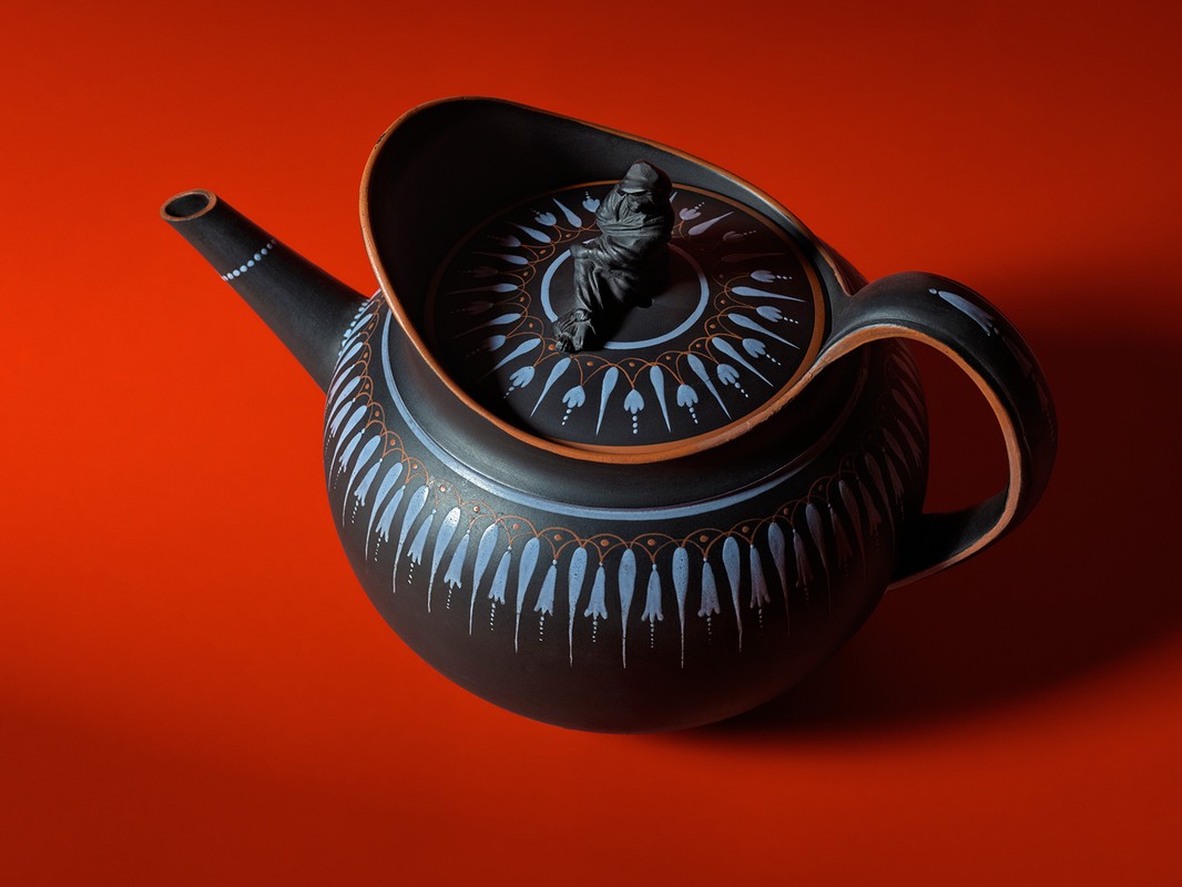 Black ceramic teapot with an intricate white and brown pattern displayed on a red background in a high-angle studio shot.