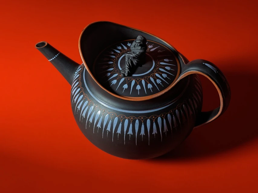 Black ceramic teapot with an intricate white and brown pattern displayed on a red background in a high-angle studio shot.