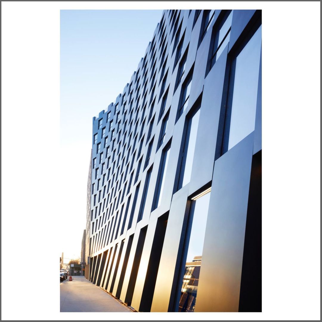 Exterior of a modern building with a curved facade and geometric window patterns against a clear sky and adjacent urban environment.