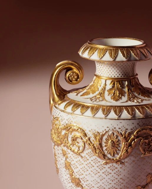Close-up of a decorative white porcelain vase with ornate gold floral accents, set against a gradient brown background.
