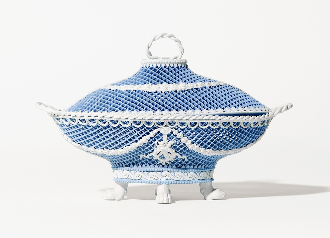 Elaborate light blue porcelain tureen with a lid, adorned with white rope-like trim and standing on small feet, against a white backdrop.