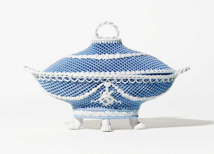 Elaborate light blue porcelain tureen with a lid, adorned with white rope-like trim and standing on small feet, against a white backdrop.