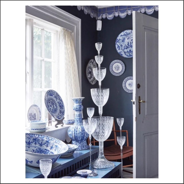 Indoor display of blue and white porcelain plates and vases on a tiered stand, with natural light streaming in from a window.