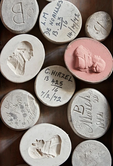 Overhead shot of a collection of round, carved stone medallions and tablets, some with portraits and lettering, arranged in a box.