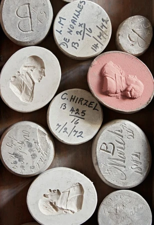 Overhead shot of a collection of round, carved stone medallions and tablets, some with portraits and lettering, arranged in a box.