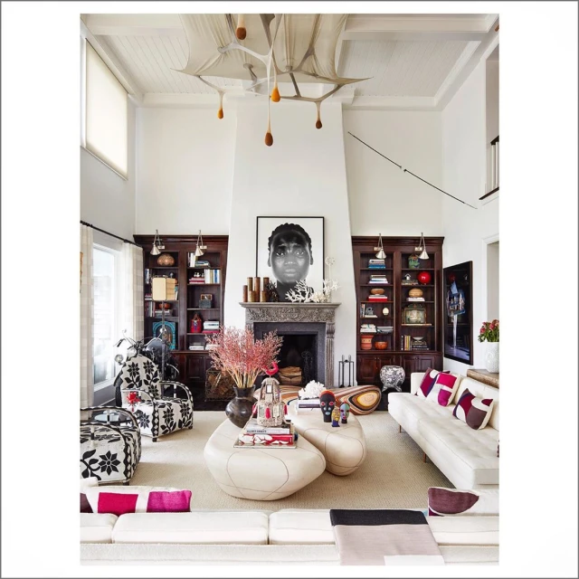 Bright living room with white couches, patterned chairs, fireplace, and decorative objects in a high-ceilinged home interior.