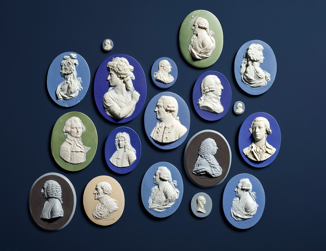 Collection of Wedgwood Jasperware cameos in varying blue, green, and brown colors against a navy background; portrait busts in profile.