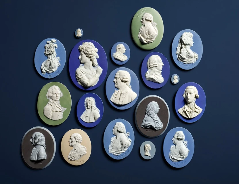 Collection of Wedgwood Jasperware cameos in varying blue, green, and brown colors against a navy background; portrait busts in profile.
