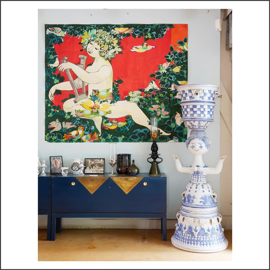 Interior view of a home showcasing a blue credenza, a decorative ceramic sculpture, and a colorful wall hanging with a reclining figure.
