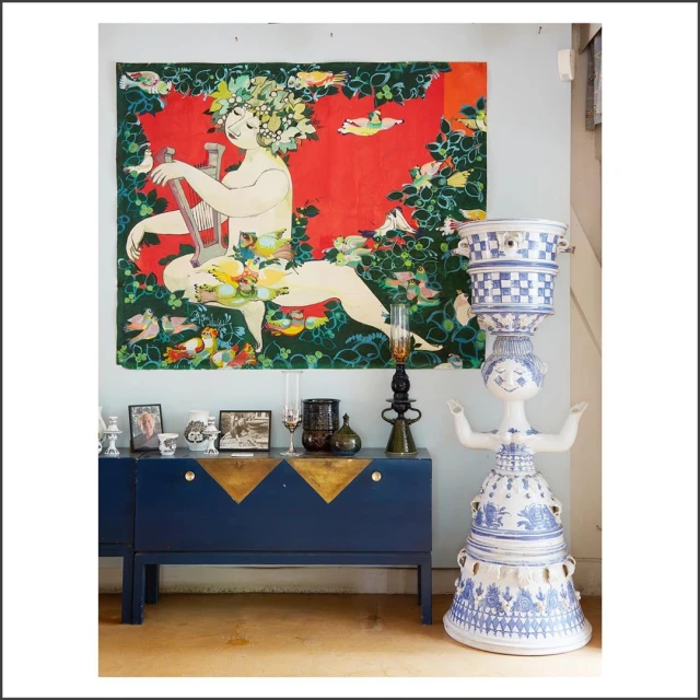 Interior view of a home showcasing a blue credenza, a decorative ceramic sculpture, and a colorful wall hanging with a reclining figure.