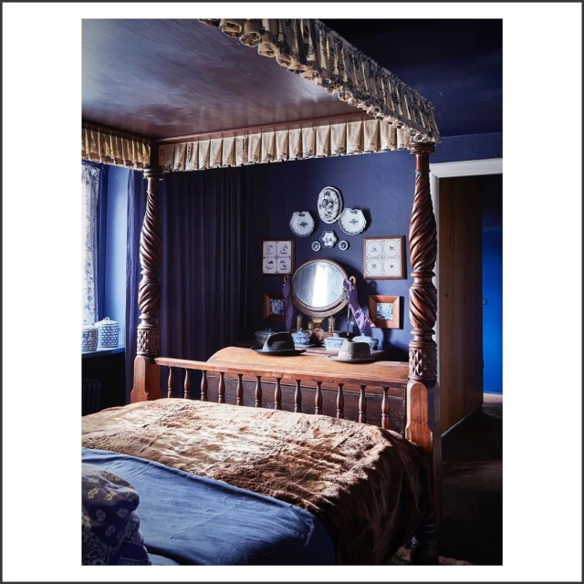 Four-poster bed in a bedroom featuring dark blue walls, wooden furniture, and decorative wall art, creating a cozy and traditional aesthetic.