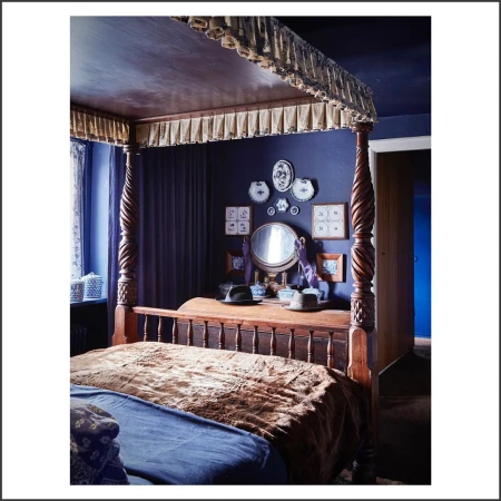 Four-poster bed in a bedroom featuring dark blue walls, wooden furniture, and decorative wall art, creating a cozy and traditional aesthetic.