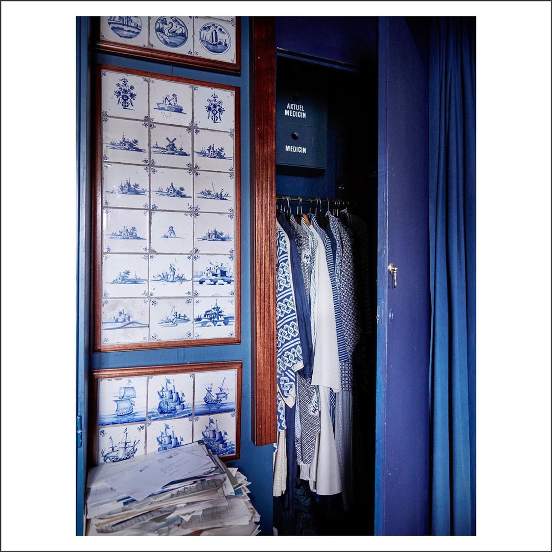 Eclectic interior showcases blue Delft tile art, a clothing-filled closet, and a pile of stacked papers creating a visually intriguing space.