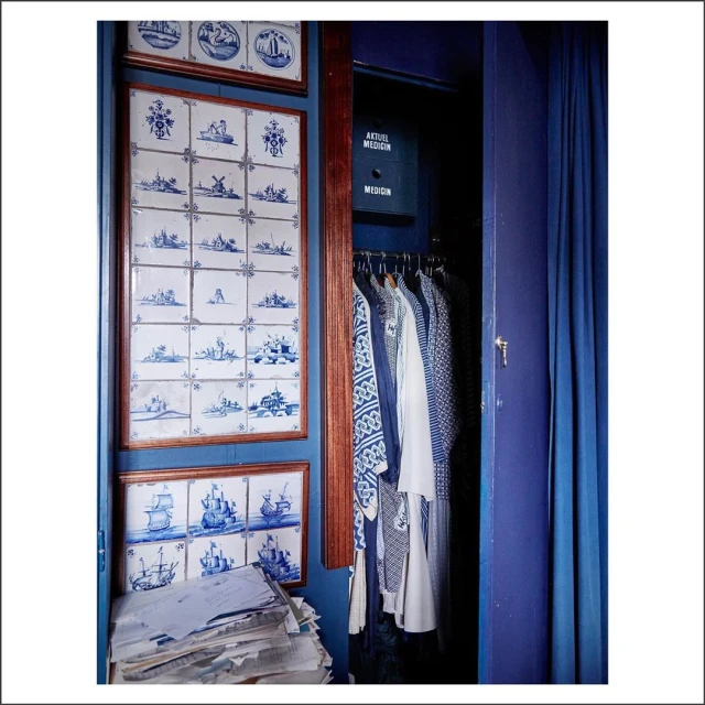 Eclectic interior showcases blue Delft tile art, a clothing-filled closet, and a pile of stacked papers creating a visually intriguing space.