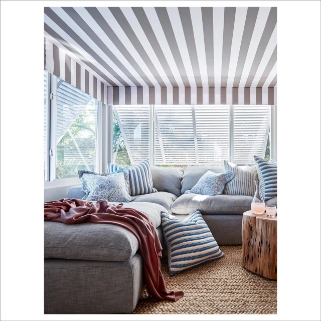 Cozy coastal living room features a gray sectional sofa with striped and patterned pillows, a wood stump table, and striped ceiling detail.