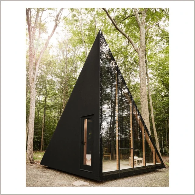 A-frame cabin with a triangular design and large glass windows nestled in a forest setting, blending modern architecture with nature.