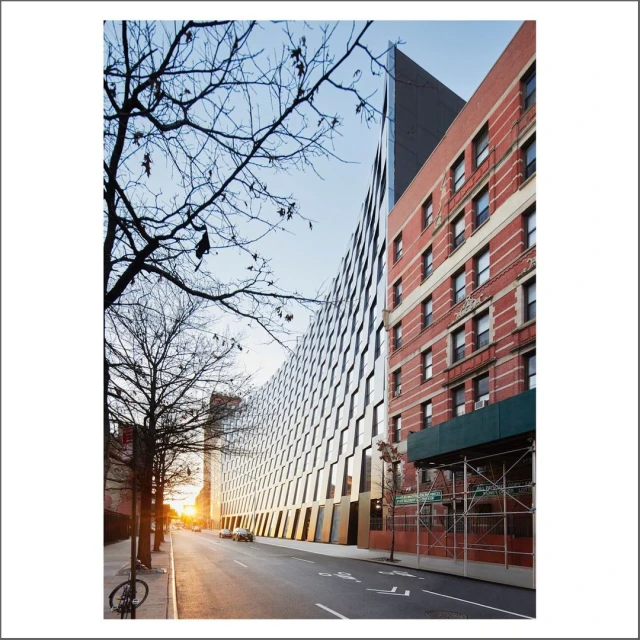Street-level view of modern architecture with curved glass facade and traditional brick building, bare trees, street, and cars.