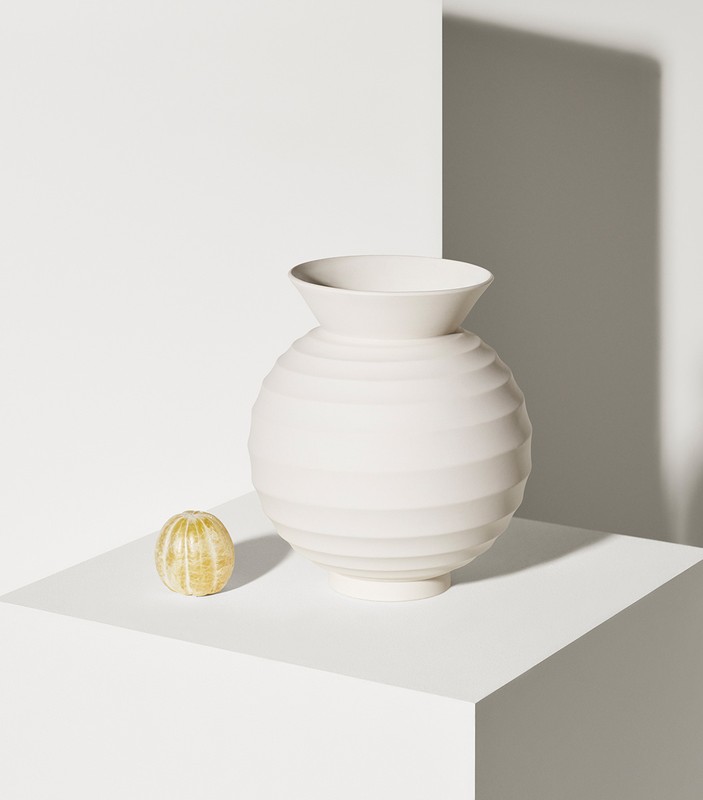 Studio shot of a white round ceramic vase beside a peeled orange on a white platform, with shadows on the white background.