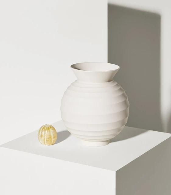 Studio shot of a white round ceramic vase beside a peeled orange on a white platform, with shadows on the white background.
