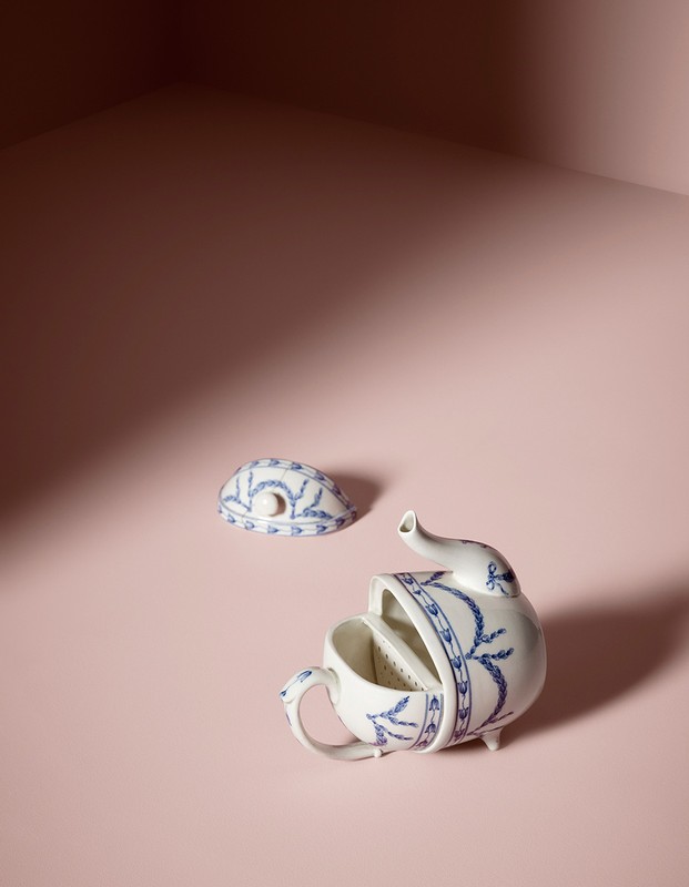 Close-up of a deconstructed porcelain teapot with blue floral patterns against a pink background and studio lighting, creating shadows.