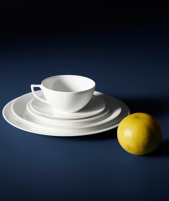 Elegant still life featuring a white teacup on matching plates and a yellow grapefruit against a deep blue backdrop.