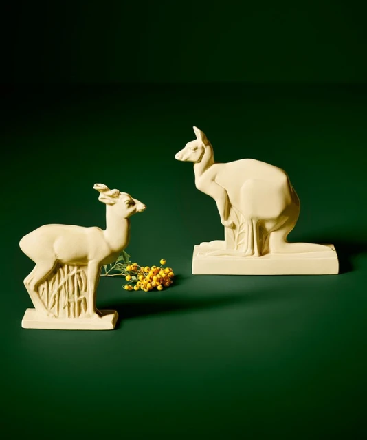 Creamy figurines of a deer and kangaroo on a green surface with yellow flowers creating a soft, natural, and whimsical aesthetic.