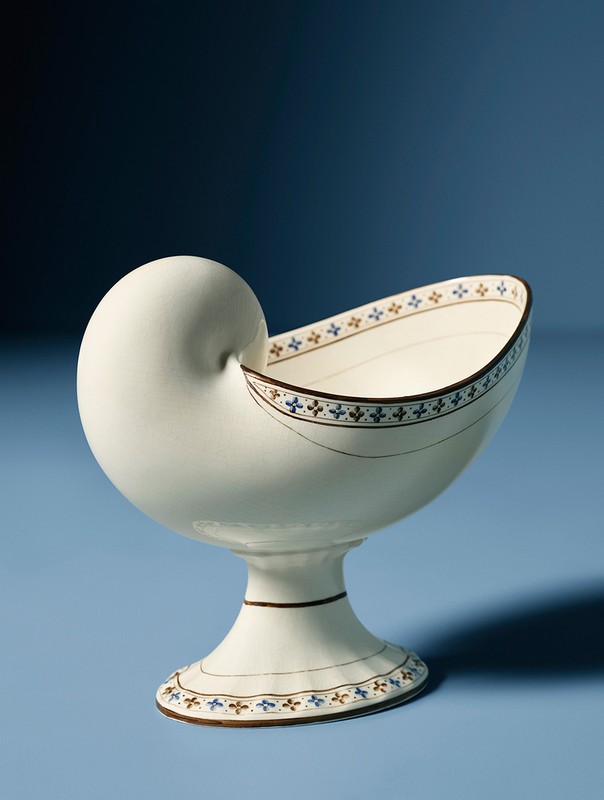 Decorative nautilus shell-shaped bowl on a blue background, featuring a detailed floral pattern and elegant pedestal design.
