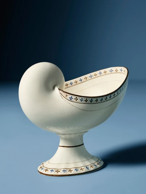 Decorative nautilus shell-shaped bowl on a blue background, featuring a detailed floral pattern and elegant pedestal design.