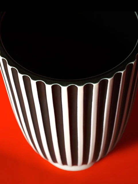 Striking still life showcases a fluted black and white ceramic pot against a vibrant orange background, emphasizing its modern design.