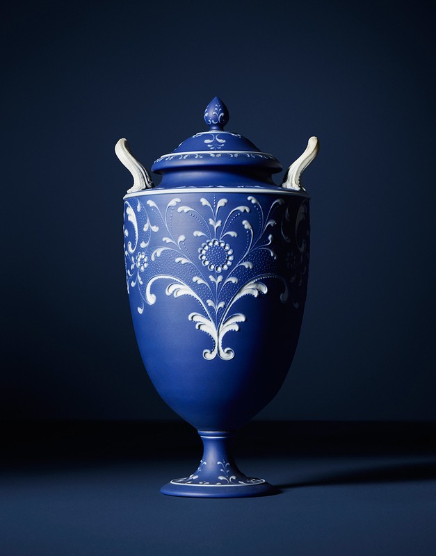 Elegant blue urn with white floral accents, featuring a matching lid, set against a dark blue background, showcasing artistic design and craftsmanship.