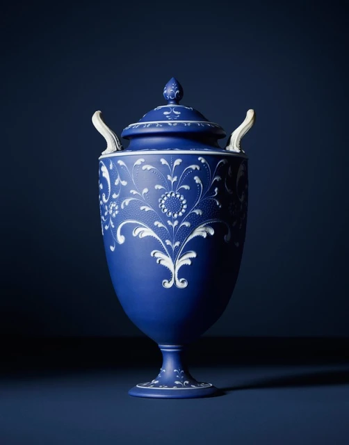 Elegant blue urn with white floral accents, featuring a matching lid, set against a dark blue background, showcasing artistic design and craftsmanship.