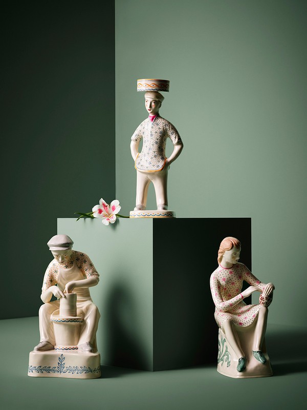 Three vintage ceramic figurines, including a potter, a seated woman, and a man with a hat, arranged on a green background with a flower accent.