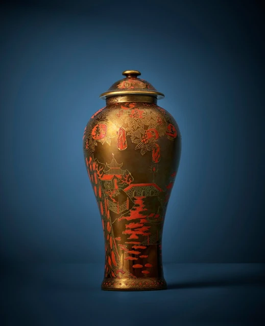 Ornate bronze vase with red detailing and a matching lid on a blue background, standing out with its intricate design and craftsmanship.