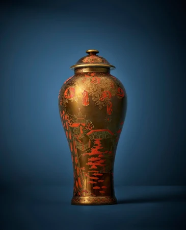 Ornate bronze vase with red detailing and a matching lid on a blue background, standing out with its intricate design and craftsmanship.