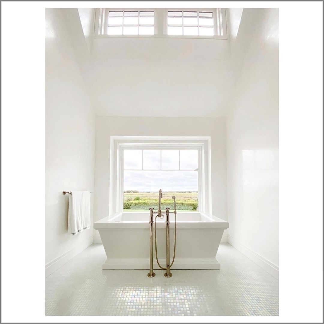 Bright and spacious bathroom interior featuring a white bathtub in front of a window offering a view of a green field landscape.