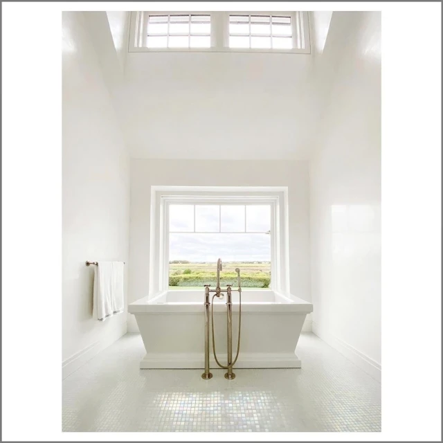 Bright and spacious bathroom interior featuring a white bathtub in front of a window offering a view of a green field landscape.