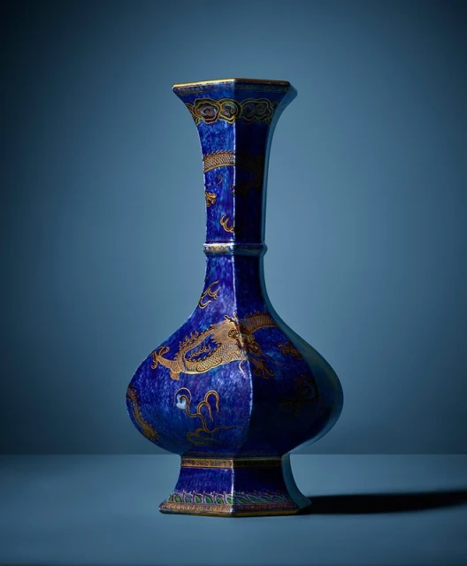 Elegant blue vase with golden dragon design on a blue surface against a blue background, ceramic craftsmanship, and ornate details.