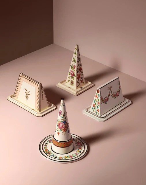 Four decorative objects with floral patterns are arranged on a pink surface, creating a visually appealing and artistic still life.