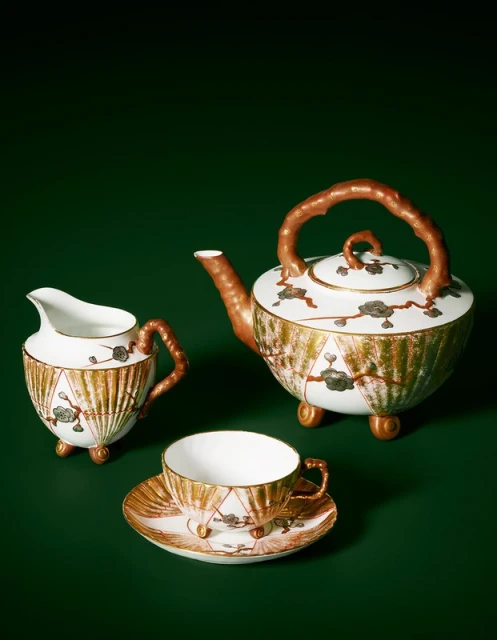 Elegant tea set with a teapot, creamer, and teacup, featuring white and gold porcelain with floral details, set against a dark green backdrop.