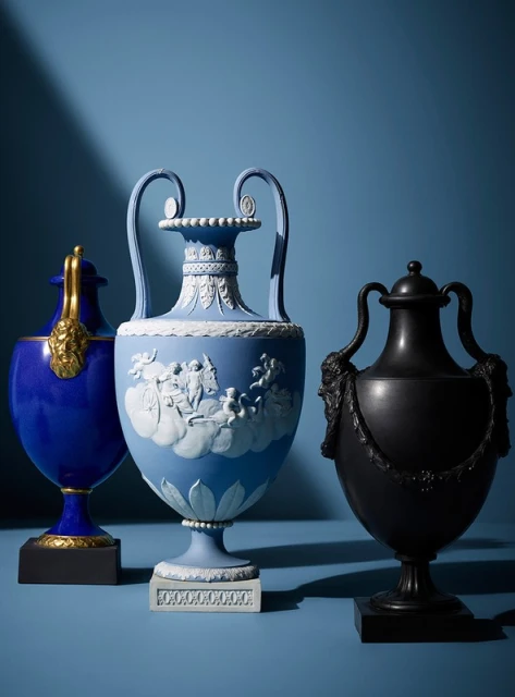 Three ornate urns of different colors, shapes, and designs are displayed on a blue surface against a blue background, studio lighting.