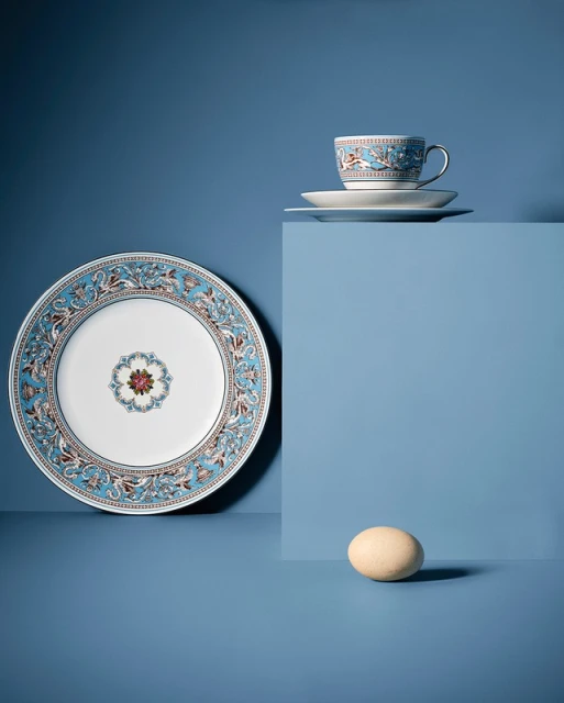 Still life of a plate, teacup, saucer, and egg on a blue surface and background creating a sense of depth and serenity.