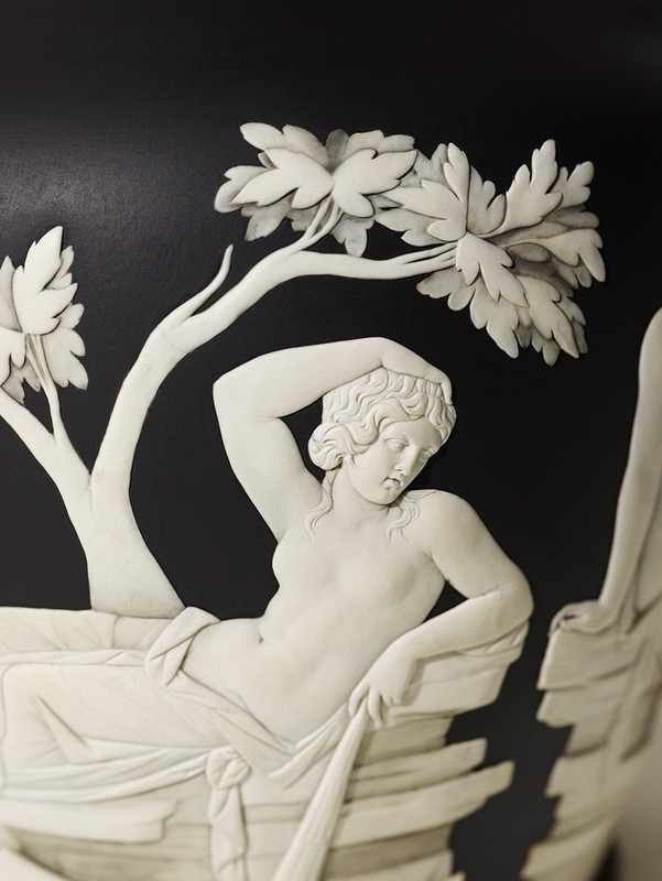 Close-up of a bas-relief sculpture on a black vase featuring a reclining nude woman under a tree. Classic art inspiration.